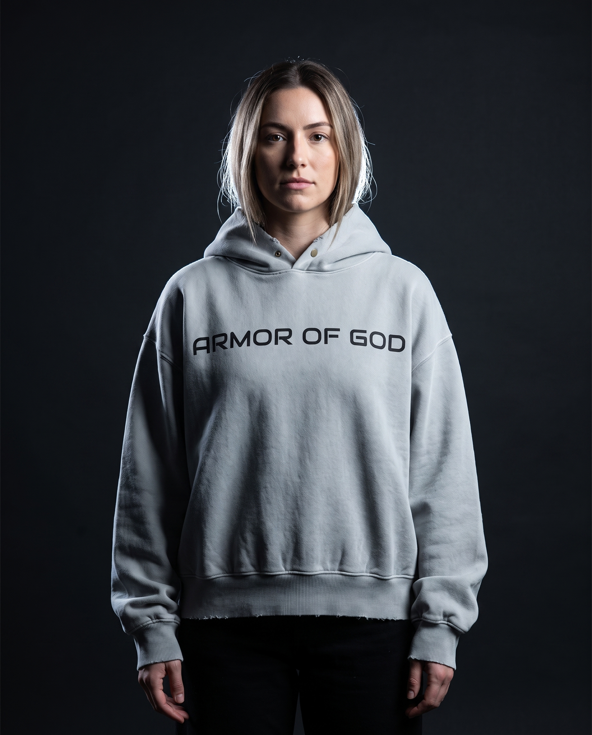 Model wearing the NPRWLR Armor of God Frayed Hoodie in light gray, front view with ARMOR OF GOD printed black across the chest, 10.3 oz enzyme-washed fleece with a frayed hem